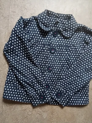 Mörkblå prickig kappa  - Snygg mörkblå kappa med vita prickar och stora knappar framtill. Jackan har en rundad krage och två fickor framtill. Perfekt för dig som vill sticka ut med en trendig look.