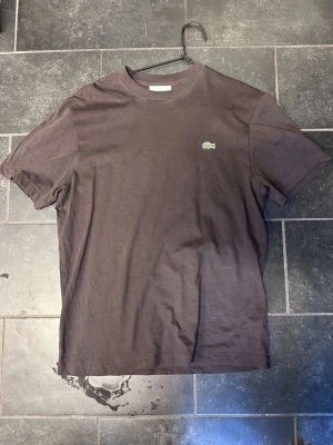 Brun  t-shirt från Lacoste - Säljer nu denna då jag knappt använder den. Den har bara hängt på en galge ända sedan jag köpte den och har aldrig kommit till användning men sitter väldigt bra och är väldigt skön 
