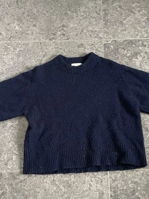 Marinblå stickad tröja - Marinblå stickad tröja med ribbade muddar vid ärmslut och nederkant. Tröjan har rund halsringning.Säljer för den har inte används på ett tag. Jättefint skick!!!