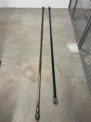 Två gardinstänger i metall 50 kr st - Säljer två gardinstänger i metall, en i svart och en i bronsfärg. Båda har dekorativa ändknoppar med mönster. Perfekta för att hänga upp gardiner och ge rummet en snygg touch.