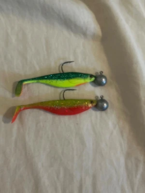 Färgglada jiggar för fiske - Säljer tre jiggar i olika färger: en grön/gul, en röd/gul och en silver/vit med rött huvud. Alla har mjuka plastkroppar och tunga jigghuvuden i metall med krok. Perfekta för dig som gillar att fiska och vill ha lite variation i beteslådan.