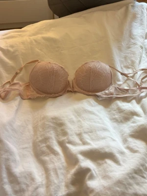 Ljusrosa spets-bh från H&M - Söt ljusrosa bh från H&M med vadderade kupor och vacker spetsdetalj framtill. Justerbara axelband och klassisk hakknäppning bak. Bh:n har en mjuk och feminin look med tunna band och diskret mönster i spetsen.