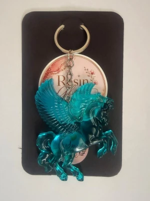 Nyckelring med Turquoise Pegasus - Snygg handgjord nyckelring med en Pegasus i transparent resin. Perfekt att fästa på väskan eller nyckelknippan för en unik och personlig touch. Metallkedja och ring i silverfärg. Finns i flera olika färger – se bilderna. Varje nyckelring säljs separat. Bilderna visar flera olika färger. Välj den modell eller färg du vill ha vid beställning.