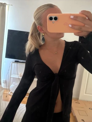 Svart omlottopp med knyt framtill - Säljer en svart omlottopp med lång ärm och knyt framtill. Toppen har djup v-ringning och är croppad, vilket ger en trendig och snygg look. Perfekt att styla med höga byxor eller kjol. Materialet känns mjukt och stretchigt.