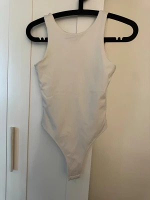 Beige basic body med hög hals - En enkel och stilren beige body med hög halsringning fram och djupare urringning bak. Tillverkad i ett stretchigt och mjukt material som sitter tight mot kroppen. Perfekt att styla till olika outfits för en clean look.