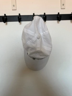 Vit keps från Sail Racing - Säljer en stilren vit keps från Sail Racing med böjd skärm och justerbar rem bak. Kepsen har broderad logga framtill och är tillverkad i ett lätt och bekvämt material, perfekt för soliga dagar.