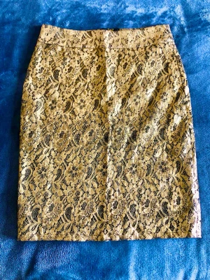 Guldspetskjol NLY Trend (Ny m. lappar) – Retro/Y2K Strl S - Superfin metallisk guldspetskjol från NLY Trend i retro/Y2K-stil! Helt oanvänd m. lappar kvar. Mjuk spets i 60% bomull & 40% polyamid med svart innertyg, synlig dragkedja och slits baktill. Perfekt till fest!                            Mått: • Midja platt: 36 cm (omkrets ca 72 cm) • Längd: 55 cm Utgången modell som ej finns i butik – perfekt för dig som söker något unikt i nyskick!