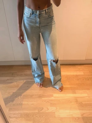 ZARA jeans  - Säljer ett par ljusblå jeans med raka ben och slitna hål på båda knäna. Jeansen har hög midja, klassisk femficksmodell och är tillverkade i denim. 