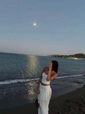 Vit strandkjol och topp set - Säljer ett snyggt strandset med en vit, axelbandslös crop top och en lång, luftig kjol i transparent material. Perfekt för strandhäng och sommarens varma dagar. Kjolen har hög midja och ett flowy fall som ger en avslappnad vibe.
