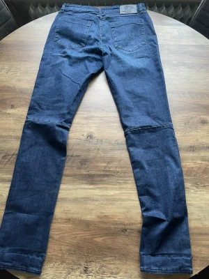  jeans från SikSilk - Säljer ett par mörkblå jeans från SikSilk med klassisk femficksdesign och läderpatch med logga bak i midjan. Jeansen har raka ben och är tillverkade i stretchigt denimtyg för en bekväm passform. 