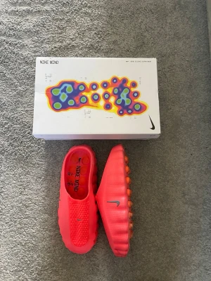 Nike Mind rosa tofflor - Nike Mind tofflor i en stark röd färg med vågig sula och ventilerande hål på ovandelen. Tillverkade i ett mjukt, skummaterial för maximal komfort. Snygg och futuristisk design med små silverfärgade Nike-loggor på ovansidan och sidan. Använda 4 gånger.