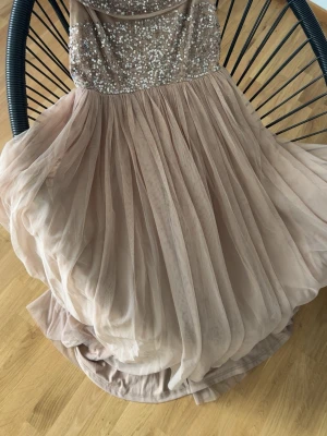 Lång champagnefärgad paljettklänning - Elegant långklänning i champagnefärg med glittrig paljettöverdel och svepande, plisserad kjol i tunt tyg. Offshoulder-modell som ger en lyxig känsla. Perfekt för speciella tillfällen där du vill sticka ut.    2 st 1 för 299 2 för 499