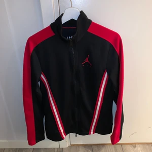 Jordan tröja - Svart jordan tröja med dragkedja och röd och vita detaljer på sidorna. Sitter lite tajt på mig som har medium och är 176cm lång. Det står att den är XS men känns som S.