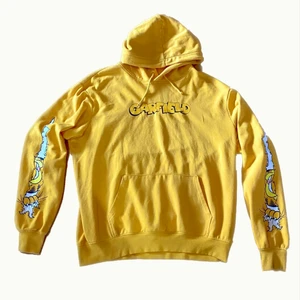 Senapsgul Katten Gustaf hoodie XL - Gul hoodie med roligt och snyggt katten gustaf-tryck på sidorna av ärmarna och baksidan och texten ”Garfield” på framsidan. Storlek XL så den sitter lite baggy om man vanligtvis har M eller L. 