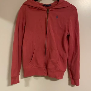 Zip up tröja från Ralph Lauren - Luvtröja från Polo Ralph Lauren. Kollar man väldigt noga så ser man på sömmarna och insidan att den har tvättats några gånger, men den är i övrigt fint skick. Den är lite mer åt det rosa hållet i verkligheten, kan ta fler bilder vid intresse. Barnstorlek 16år/XL, passar xxs-s beroende på hur man vill att den ska sitta.
