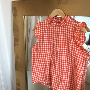 rutig blus  - orange/ vit rutig blus, supergullig och lite lantlig, söta volanger vid axlarna! fråga om ni undrar något, köparen står för frakten:) 