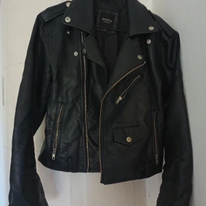 Svart biker jacka från Barneys originals. FRI FRAKT! - Svart biker jacka i fuskläder från märket Barneys Originals. Tyget har sprätt upp på insidan som syns på bild tre men detta är ingenting som syns från utsidan. Strl 8. Alltid fri frakt.