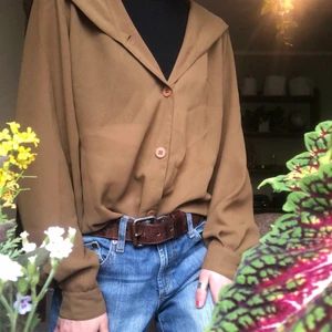 Blus - En olivfärgad blus från märket Mexx i tunn polyester.  Har tunna axelvaddar och krage som övergår till luva. Går att stylea både öppen och stängd. Mycket fin!