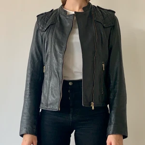 Svart skinnjacka från Zara storlek 36 - Svart äkta läderjacka från Zara i storlek 36, men skulle även säga att den passar en 34a. Har gulddetaljer, två fickor framtill och quiltat tyg. Väldigt bra skick! Köpare står för frakt.