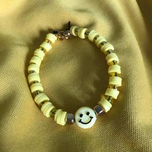 Armband med gula claybeads, små gula pärlor, guldiga pärlor, en smiley och svart tråd! Cirka 15 cm!