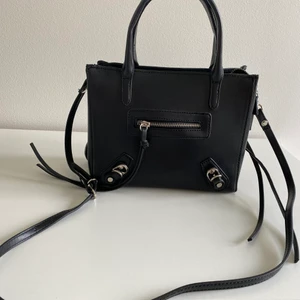 Svart väska från Nelly  - Helt ny väska från Nelly. nypris 399 kr  Läderimitation Avtagbar och justerbar axelrem Dubbla handtag Försluts med dragkedja Fodrad insida Mindre innerfack med dragkedja Litet Ytterfack med dragkedja Dragkedjor i sidorna Mått: Bredd 24 cm, Höjd 18 cm, Djup 11 cm