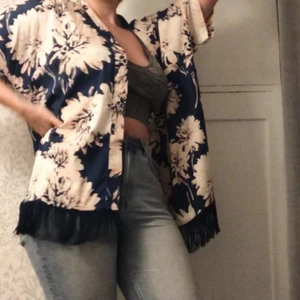 Blommig kimono med vacker fransrad - Fantastisk kimono med stort blommönster. Kimonon är ifrån AVA JUNE i storlek 34, den är dock stor och luftig så skulle passa upp till 42-44 beroende vilken passform man är ute efter. Älskad men bara använd en gång.