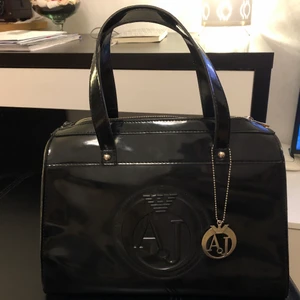 Armani Jeans AJ svart väska  - Väldigt snygg och i fint skick. Lite glänsande lackliknande med logo. Finns 2 små fickor på insidan och en på utsidan 