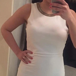 Vit kort klänning  - Väldigt fin vit kort klänning med guld detaljer både i halsen och i ryggen. Den passar perfekt till både student och fest. Den är i strl: 38. Klänningen är i ny skikt 