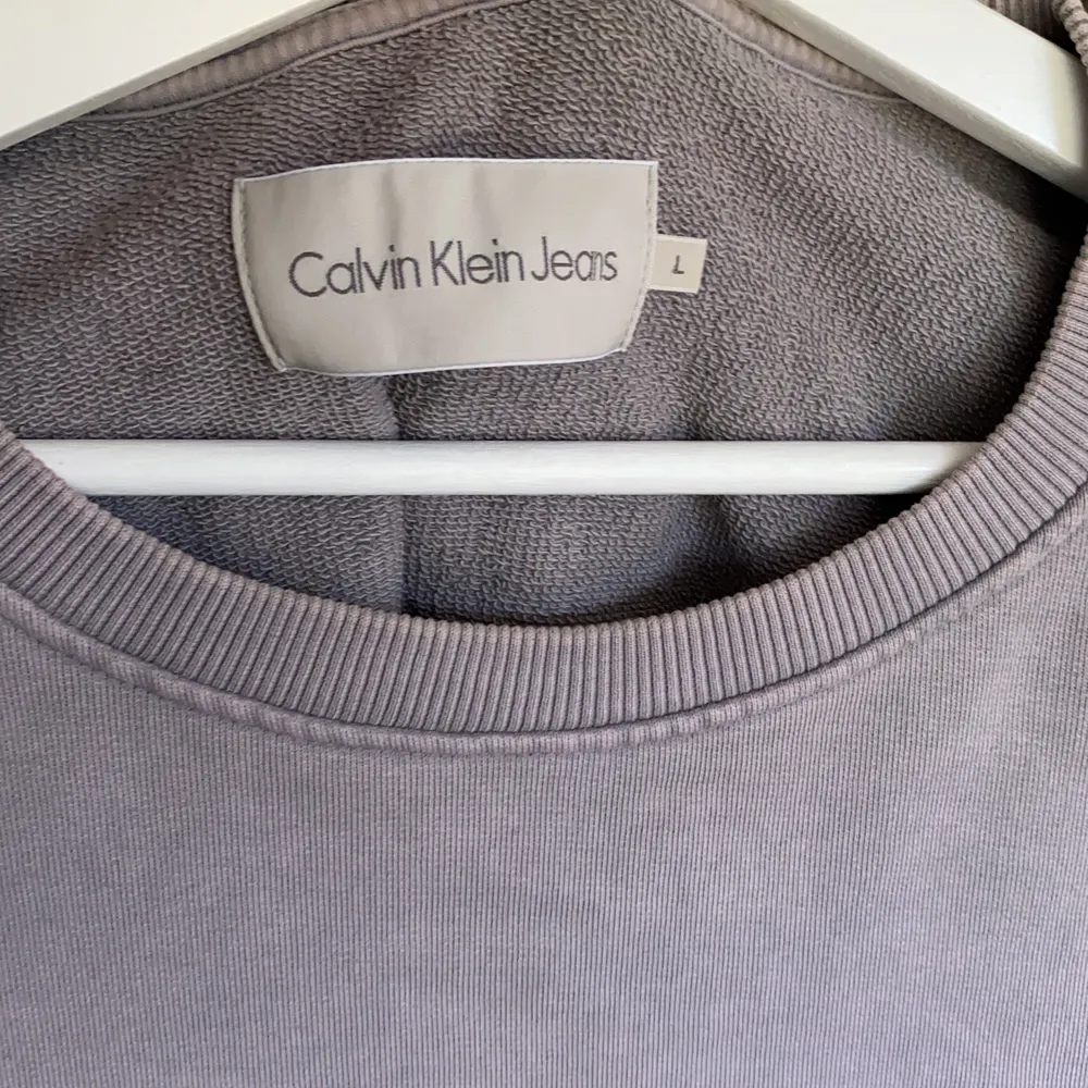 Stengrå sweatshirt med svart tryck på magen från Calvin Klein Jeans. Använd 5 gånger och inköpt förra året. Strl L och passar mig perfekt som är 188/78kg. . Tröjor & Koftor.