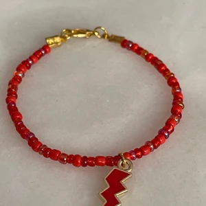 Red lightning  - Super fint armband i tre olika röda färger och med en röd blixt berlock i mitten. Bandet är elastiskt och man kan välja mellan olika storlekar. Ingår spänne och ringödlor så man kan justera det efter önskad storlek.