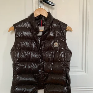 Moncler väst dam  - Jättefin brun väst från Moncler. Knappar framtill samt två fram fickor.  Mycket fint skick!  Västen är inköpt på Vestiare Collective som är en hemsida för begagnade märkeskläder så den är helt äkta!   Varan skickas när pengarna sitter på kontot!