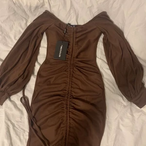 Pretty little thing klänning - Plt klänning i en brun färg i storlek 6 helt ny och oanvänd prislappen finns kvar säljer för 200. Kunden står för frakten.