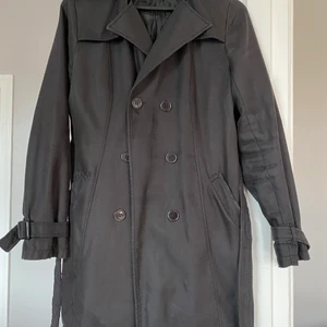 Svart trenchcoat  - Svart trenchcoat - använd men i ok skick. Fodret i ena fickan är trasigt, går enkelt att laga själv eller leva med :) 