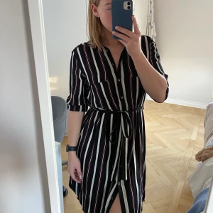 Randig Skjortklänning från Lindex - Säljer denna randiga skjortklänning i färgerna svart, vit och orange från Lindex. Den är knappt använd och i mycket gott skick. Storleken är S.  Frakt tillkommer om inget annat är överenskommet ☺️