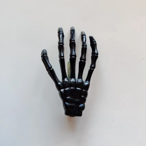 Skelett hand hårklämma - En svart hårklämma som ser ut som en skelett hand och är i bra skick. Vet inte vart den är köpt då jag fått den. Från långfingret på klämman är den 8 cm lång. (Köparen står för frakten)