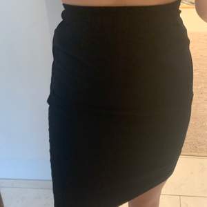 Svart kjol med två lager i fint tyg med slits i bak. Snygg passform och formar kroppen fint. 
