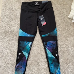 Oanvända tights från Reebok - Snygg tights från Reebok, aldrig använda så helt i nyskick! Säljer pga passar inte mig. Stilrena blå detaljer och mönster på vaderna som syns på bild 2. Spårbar frakt med DHL inräknad i priset!