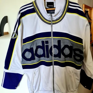 Adidas vintage tröja  - Vintage adidas tracksuit. Top jacket zip up fleece coat. Three strikes.  Limited add. D 7 , F 186   Vit, blå och gul med stora klassiska logobokstäver.   Armarna på tröjan kan man välja att ha kortare eller längre. Två fickor med dragkedja.  Se bilder.  Har använts, men har behandlats väl och är ännu fräsch och i bra skick!