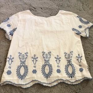 Vit blus - En vit blus med blåa detaljer. I bak på blusen finns det en knapp vid nacken som detalj. Blusen är i bra skick och syns inte att den är använd. 