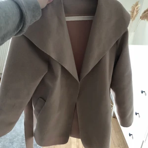 Beige kappa  - beige kappa i ett skönt material. Lite kortare modell med tillhörande band i midjan. Perfekt nu till våren! Storlek M.  Köpt för 549kr.