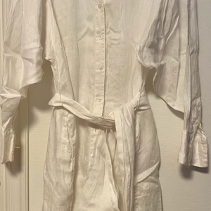 Linneklänning - Vit skjortklänning i linne med ballongärm, skärp i midjan slutar nedanför knäna 