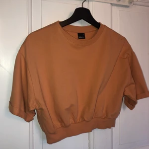 Orange Kroppad T-Shirt Gina Tricot - En supersnygg kroppad t-shirt i en diskret orange färg. Ärmarna är uppvikta och modellen är lite overzised. Använd 3 gånger och därmed i fint skick. Köparen står för frakt! 
