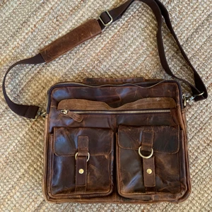 Brun axelremsväska - Använd bara ett par gånger, i nyskick. Säljer pga. föredrar ryggsäck. Rymmer lätt A4 och dator och ett par böcker. Två stora fack och ett par små inuti och utanpå. 