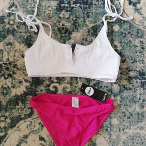 Oanvänd bikini med mörk rosa trosor och vit ribbad överdel med knytning på axlarna och tryck knappar. 