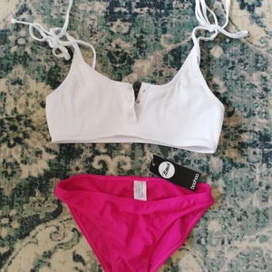Bikini strl. 36 - Oanvänd bikini med mörk rosa trosor och vit ribbad överdel med knytning på axlarna och tryck knappar. 