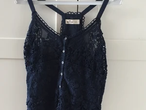 Mörkblått linne i spetsliknande material - Jättegulligt marinblått linne från hollister. Sitter tyvärr lite tajt så väljer att sälja. Storlek S, funkar eventuellt på M. Kontakta mig vid intresse eller bild på hur den sitter❤️ Frakt tillkommer.