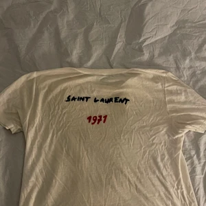 Saint Laurent T-Shirt storlek L  - Vit Saint Laurent t-shirt med tryck på ryggen, storlek L men är rätt liten i storlek så sitter även bra om man har M 