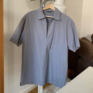 ljusblå/grå tshirt-skjorta - Oversized prasslig skjorta storlek L, lite cos-aktig! Två små dragkedjor, undre blir till en ficka. Väldigt bra skick! härligt material. Funkar både på herr och dam!