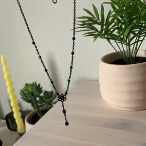 Svart halsband - Svart halsband med en blomma och en liten hängande ”charm”.                                                                                     Säljes pga inte min stil längre.                                                 20kr+frakt