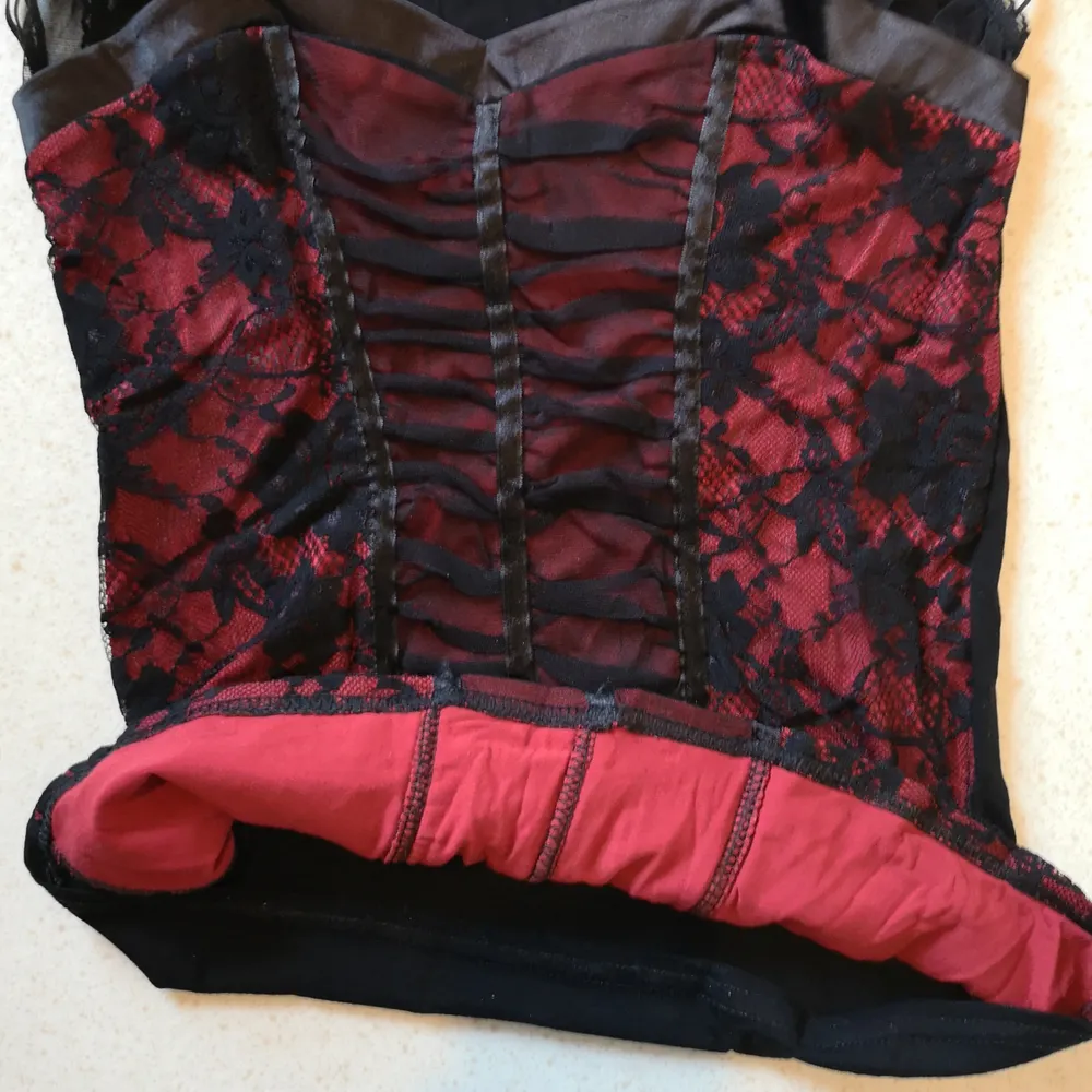 Rött-svart plagg i korsett-stil med fina genomskinliga ärmar på axlarna. Sitter fint på kroppen! Pris är inklusive frakt 😊. Toppar.